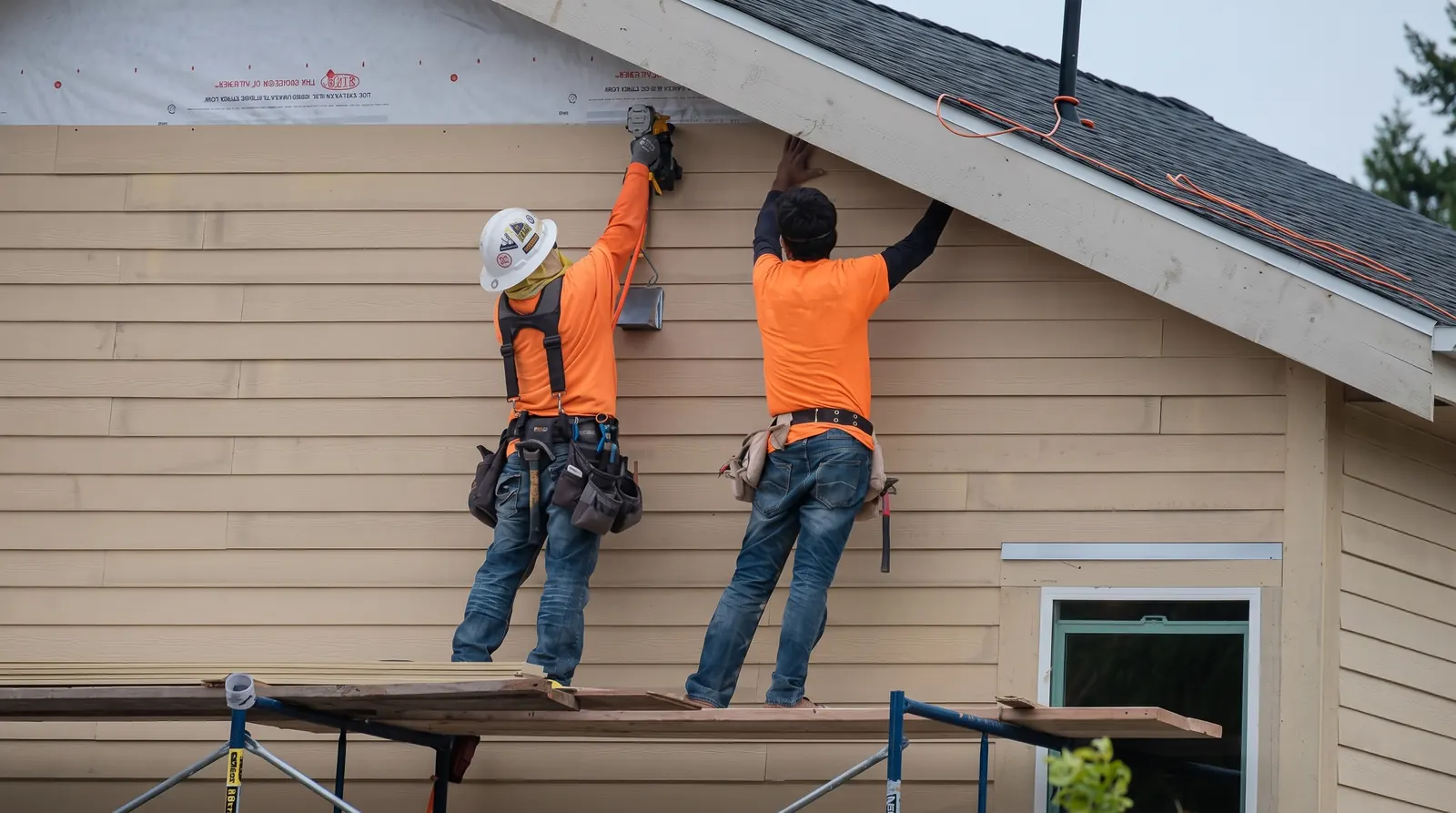 Two workers installing horizontal siding beneath a residential roofline